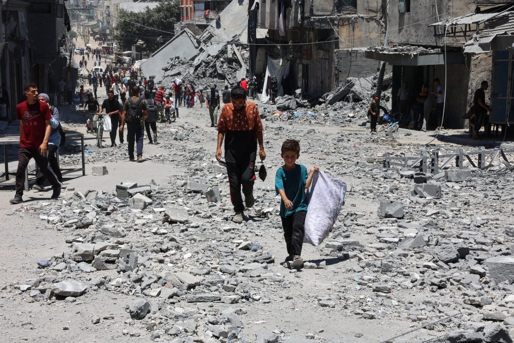 فلسطينيون يسيرون أنقاض مبانٍ دُمّرت جراء غارات إسرائيلية على حي الدرج في غزة (أ ف ب)
