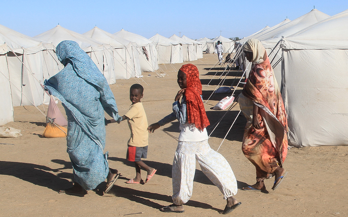 عائلة سودانية تسير أمام خيام في مخيم العفاد للنازحين في بلدة الدبة شمال السودان (أ ف ب)