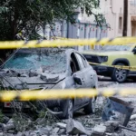 سيارة محطمة بالقرب من مبانٍ متضررة بعد اعتراض طائرة مسيرة إيرانية في البحرين (رويترز)