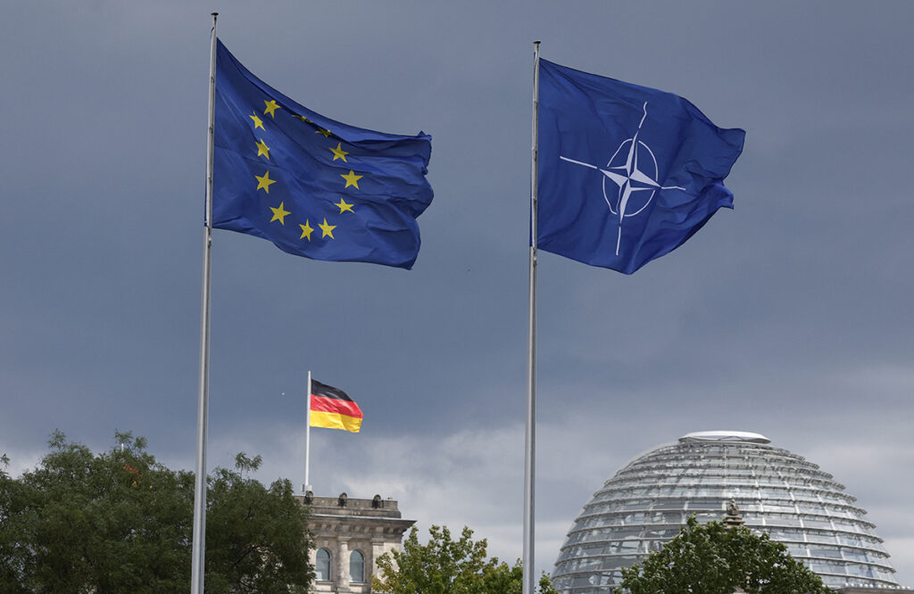 The EU, German and NATO flag fly backdropped by the Reichstag building that houses the Bundestag (lower house of Parliament) ahead a ceremony to mark Germany's 70 years in NATO in Berlin, on July 9, 2025. (Photo by Odd ANDERSEN / AFP)