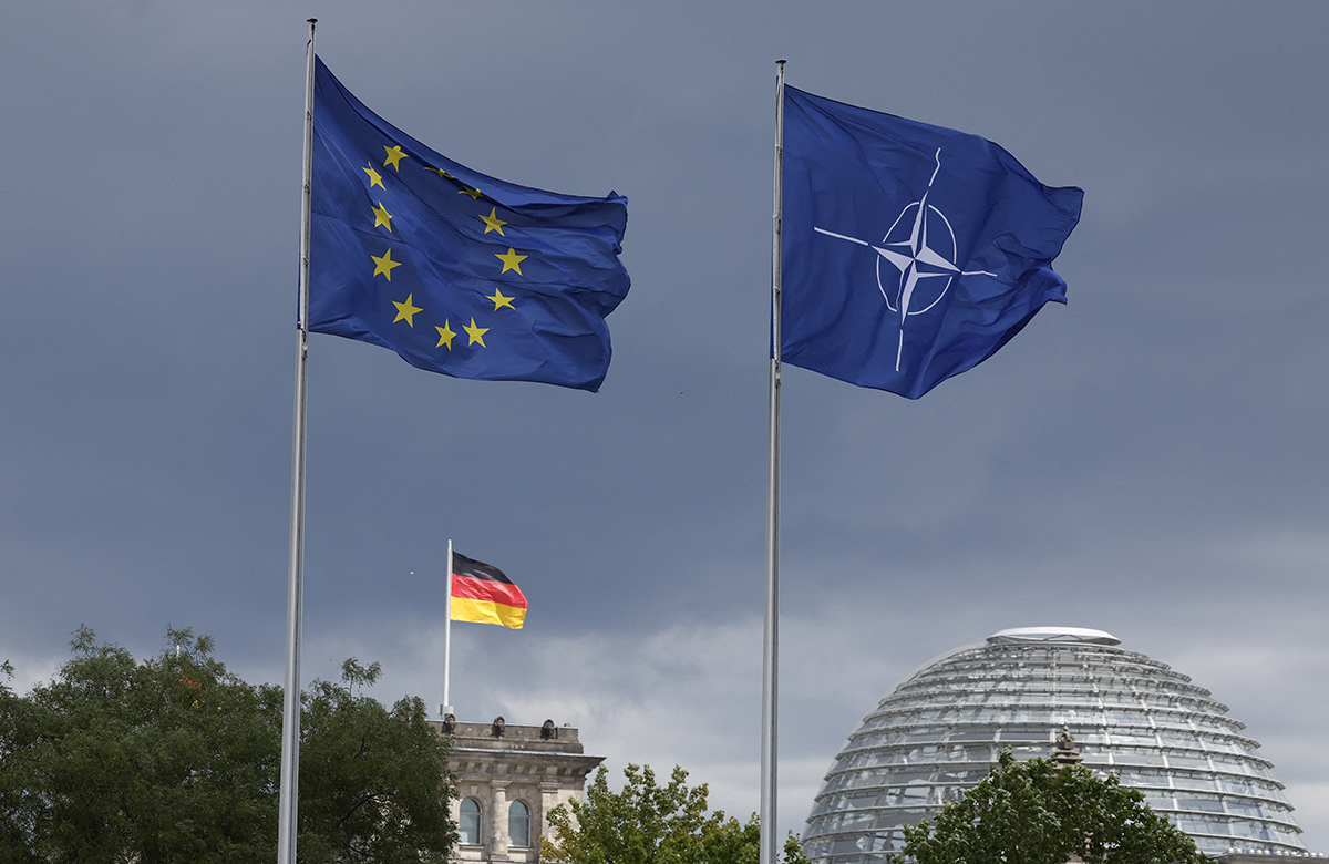 The EU, German and NATO flag fly backdropped by the Reichstag building that houses the Bundestag (lower house of Parliament) ahead a ceremony to mark Germany's 70 years in NATO in Berlin, on July 9, 2025. (Photo by Odd ANDERSEN / AFP)