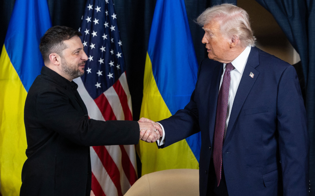 Ukrainian president Volodymyr Zelensky shakes hands with U.S. president Donald Trump in front of the Ukrainian and American flags.