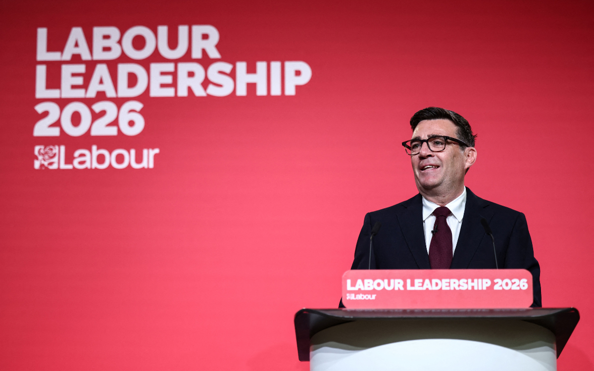Andy Burnham giving a speech at a desk in front of a red background which reads "Labour Leadership 2026"