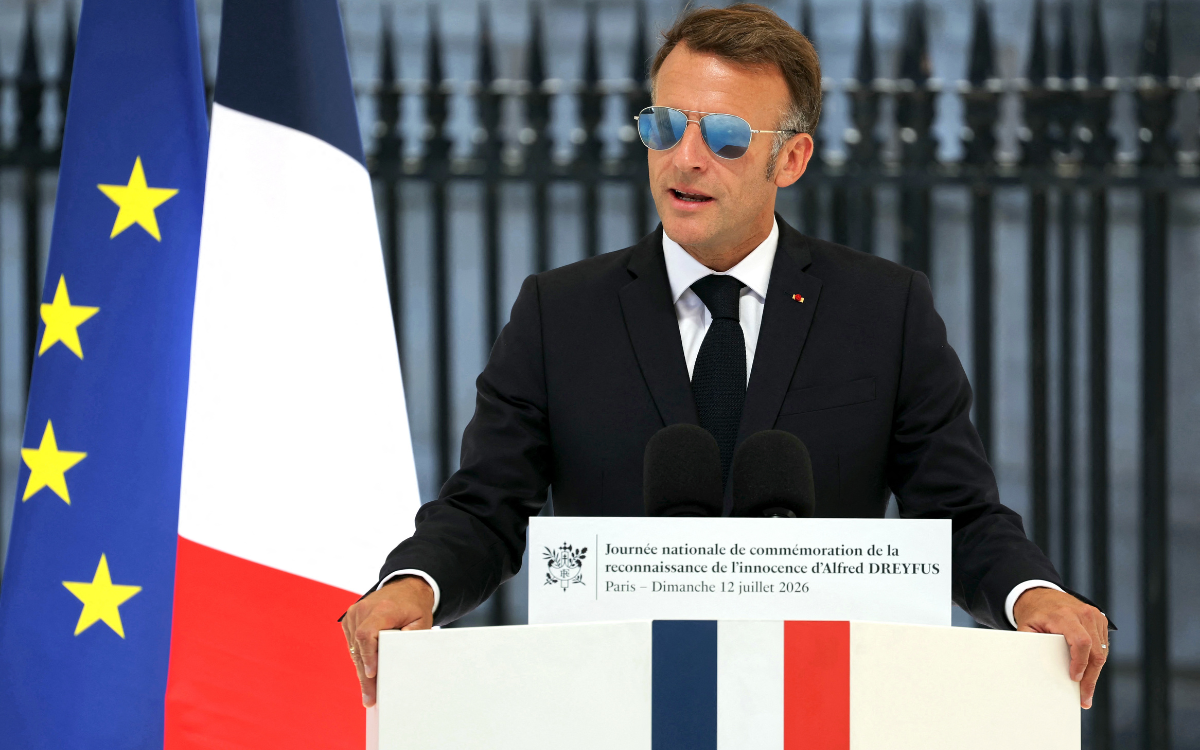 French president Emmanuel Macron wearing sunglasses during a speech in front of a desk with the French flag and with France's and the European Union's flags behind him
